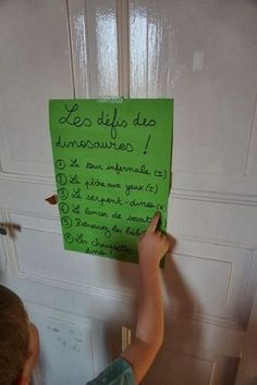 a young boy writing on a green piece of paper that is attached to a door