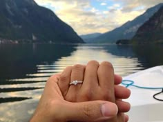 two hands holding each other while standing on a boat in the water with mountains in the background