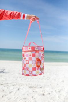 a person holding a pink and white checkered bag on the beach with blue skies in the background