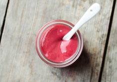 a glass jar filled with red liquid on top of a wooden table next to a white spoon