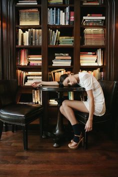 a woman sitting at a table in front of a bookshelf