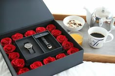 a black box with red roses in it sitting on a bed next to a cup of coffee