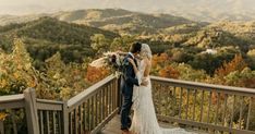 a bride and groom kissing on a deck overlooking the mountains