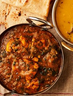 some food is sitting in a bowl on a table next to pita bread and soup