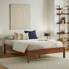 a bed sitting in a bedroom next to a wall mounted book shelf and lamp on top of a wooden floor