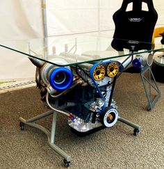 a glass table with an engine on it in front of a white wall and black chair