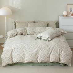 a bed with white and green comforters in a room next to a lamp on the floor