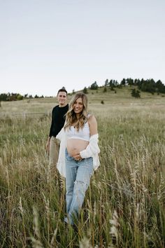 a pregnant woman standing next to a man in a field