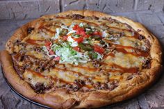 a pizza sitting on top of a metal pan covered in cheese and toppings next to a brick wall