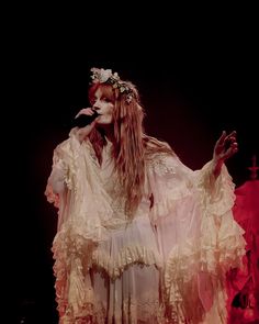 a woman with long hair wearing a white dress and holding her hands out in front of her face