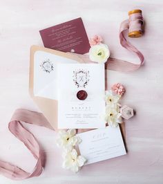 the wedding stationery is laid out with ribbon, flowers, and rings on it