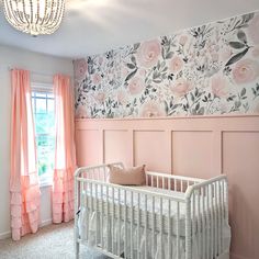 a baby's room decorated in pink and gray with floral wallpaper, crib bedding, and chandelier