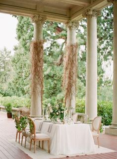 the table is set up for an outdoor dinner party with white linens and greenery