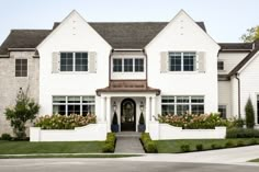 a large white house with lots of windows and plants on the front lawn in front of it