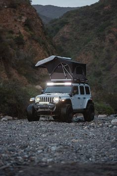 a white jeep with its lights on is parked in the middle of a rocky area