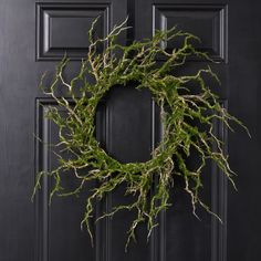 a wreath with green moss hanging on a black front door, next to a brown wooden door