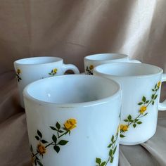 three white cups with yellow flowers painted on the sides and green leaves in the middle