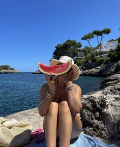 a woman sitting on top of a beach next to the ocean wearing a watermelon hat