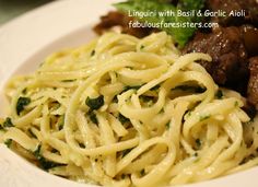 a white plate topped with pasta and meat next to greens on top of a table