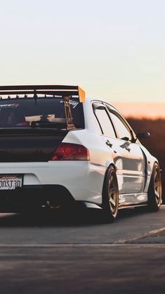 the back end of a white car parked on top of a parking lot at sunset