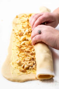 a person is rolling out some food on a white counter top with their hand resting on the rolled up dough