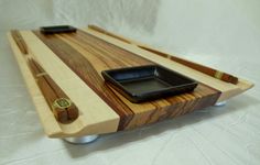 a wooden tray with chopsticks and a black bowl on the bottom is sitting on a white sheet