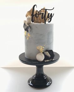 a black and white cake with gold leaf decorations on it's top is decorated with the word forty