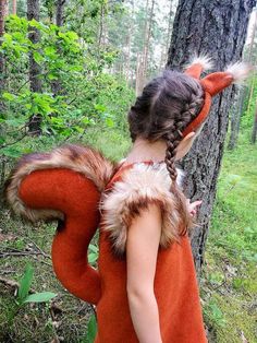 a woman in an orange dress standing next to a tree and wearing a fox tail