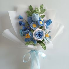 a bouquet of crocheted flowers with blue and yellow accents on white wrapping paper