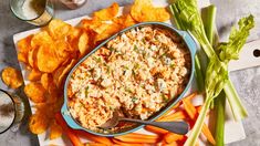 a bowl of dip surrounded by carrots and celery next to some chips