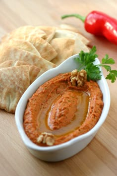 a bowl of hummus and pita bread on a wooden table with red peppers