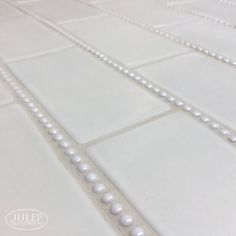 a close up view of a white tile with pearls on the bottom and one bead at the end