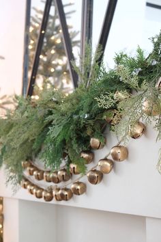 a christmas tree with bells hanging from it's branches and garland on the mantle