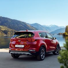 the rear end of a red car parked in front of a lake