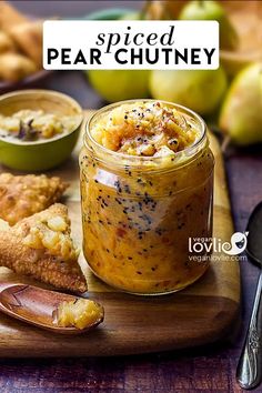 a wooden cutting board topped with food and a jar filled with pudding next to two spoons