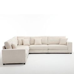 a white sectional couch with pillows on it's back and side facing the camera