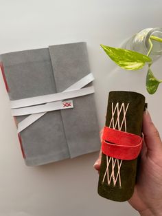 a hand holding a rolled up piece of paper next to a green plant and gray notebook