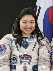 a woman in an astronaut's suit standing next to a flag and smiling at the camera