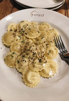 a white plate topped with pasta covered in cheese and seasoning next to a fork