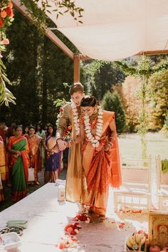 a couple getting married in front of an outdoor wedding ceremony with flowers and garlands