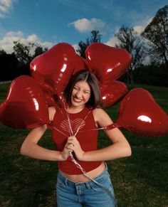 a woman holding red balloons in the shape of heart's on her chest and smiling at the camera