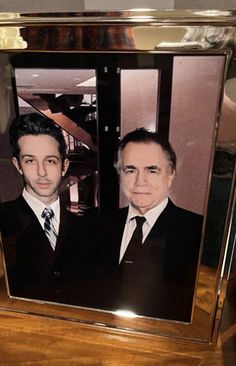 two men wearing suits and ties are in a wooden frame on a table next to each other