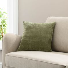 a green pillow sitting on top of a beige couch next to a white window sill