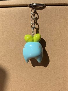 a blue and green elephant keychain hanging from a brown cardboard box with a chain attached to it