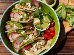 a green bowl filled with tacos and veggies next to a wooden cutting board