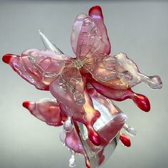 a pink flower made out of glass sitting on top of a metal stand in front of a gray background