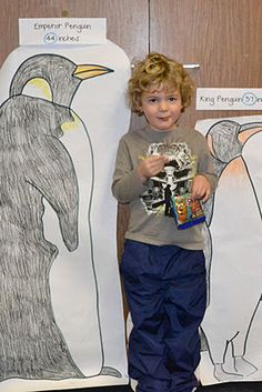 a young boy standing in front of two paper cut outs with penguins on the side