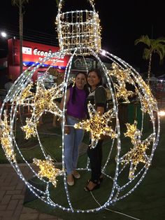 two women standing next to each other in front of a christmas ornament with lights on it