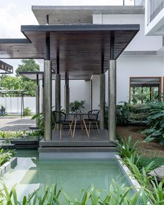 an outdoor dining area next to a pool with chairs and tables on it, surrounded by greenery