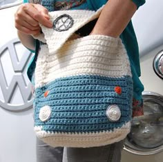 a woman is holding a crocheted purse in front of a vw bug